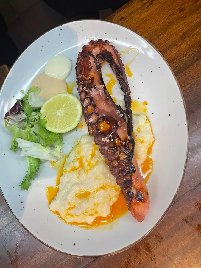 Pata de pulpo a la brasa sobre huevos rotos, con lima y ensalada